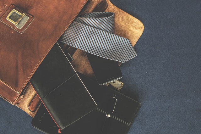 Kožená pánska taška, z ktorej vypadávajú peňaženka, tablet a kravata.jpg